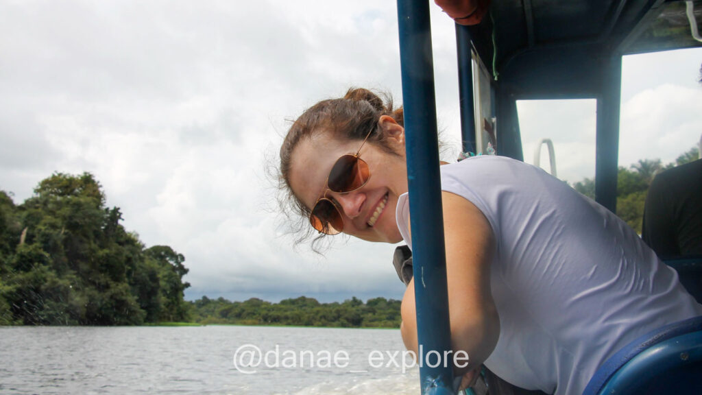 Eu, uma mulher branca, com óculos de sol e camiseta branca, debruçada na lateral de um barco, olhando para trás para câmera, enquanto o barco navega pelas águas do Rio Negro, próximo ao Parque Nacional Anavilhanas