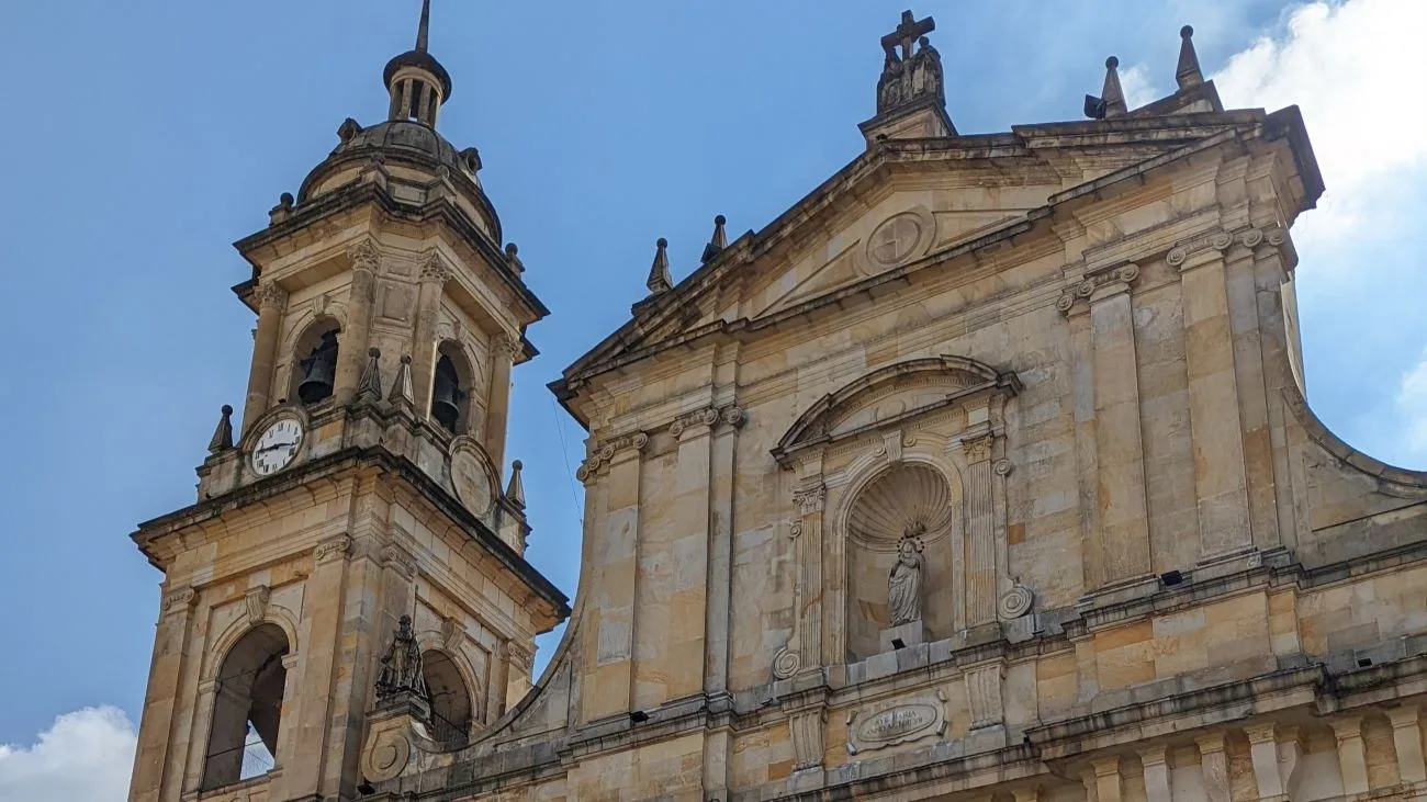 Facade of the Catedral Primada de Bogotá, with its clock tower and stone details under a blue sky.