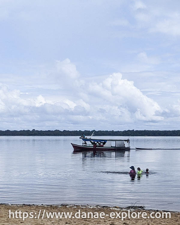 crianças brincam no Rio Negro, com barco ao fundo, em dia nublado, parte de nosso roteiro para visitar a Amazônia Brasileira no Parque Nacional de Anavilhanas