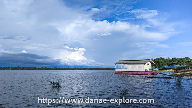 Casa típica de madeira da amazônia, branca com portas e janelas vermelhas e uma garota na varanda. Novo Airão, uma das paradas de nosso roteiro para visitar a Amazônia Brasileira no Parque Nacional de Anavilhanas