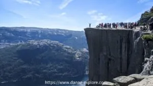 turistas posando para fotos e admirando a vista no topo da Preikestolen, a Pedra do Púlpito, na Noruega, em dia de sol e céu azul
