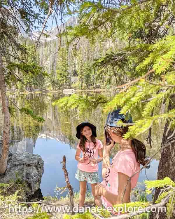 Two girls taking a photo by a lake in Rocky Mountain National Park, Bear Lake region