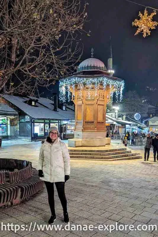 Young woman in winter clothes, with hat and gloves, in front of Sebilj Fountain in Sarajevo, part of what to do in Sarajevo in 1 or 2 days