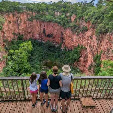 Plataforma de observação do Buraco das Araras, Bonito - MS. Familia de costas, olhando para o buraco, se observa a vegetação no fundo do buraco, as pareces rochosas, vegetação acima do burado e céu encoberto, um dos passeios mais legais da nossa lista do que fazer em Bonito em 4 dias