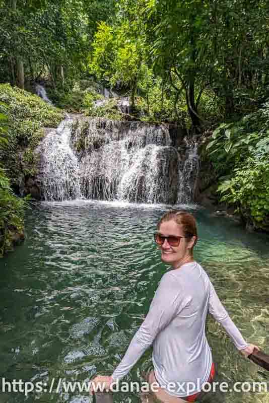 Moça em camiseta branca e óculos de sol olhando para câmera, em frente a cachoeira em Bonito, parte de nosso guia com tudo que você precisa saber para visitar Bonito, no Mato Grosso do SUl