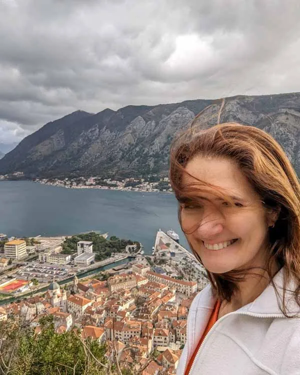 Selfie na Fortaleza de Kotor - mulher branca, cabelos longos, com vista ao fundo da cidade antiga de Kotor, Baia de Kotor e montanhas ao fundo, em dia nublado