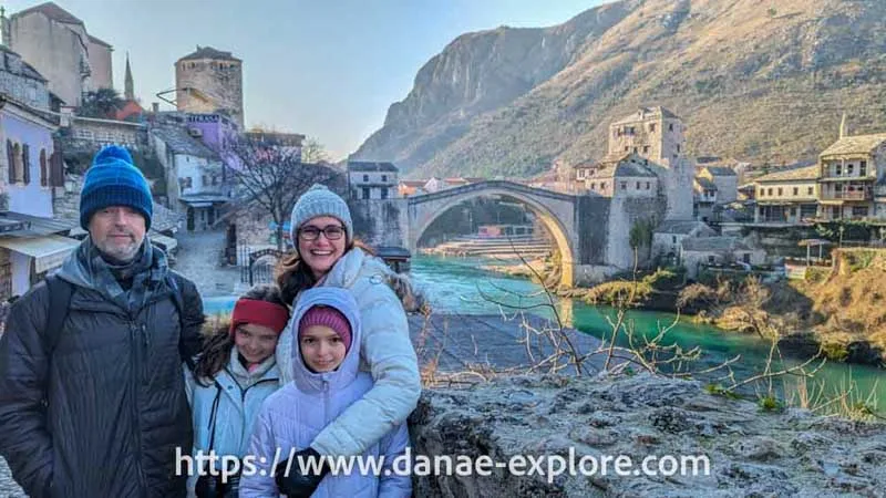 Tourists in winter clothes smiling in front of the iconic Stari Most bridge in Mostar, Bosnia and Herzegovina.