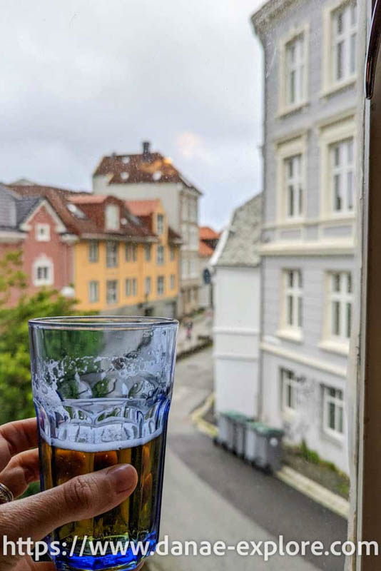 Copo de cerveja em frente a uma janela, ao fundo, ruas de Bryggen, Bergen, Noruega