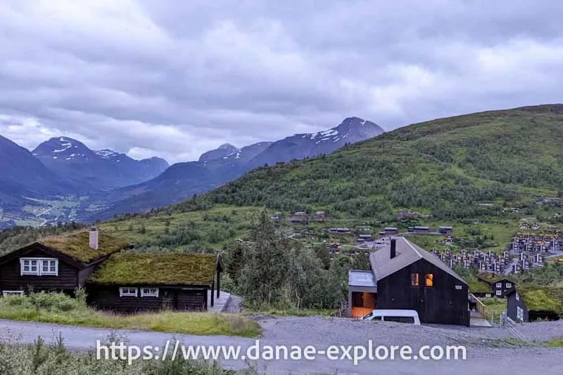Casas de madeira escura, com teto ajardinado, em vale com vegetação verde e montanhas com um pouco de neve ao fundo. Noruega, é caro viajar na Noruega?