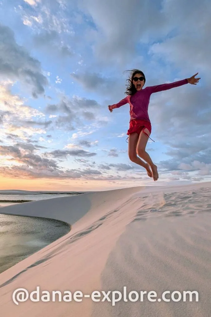 jovem pula em duna, ao por do sol, com os braços abertos, sorrindo, em Lençóis Maranhenses
