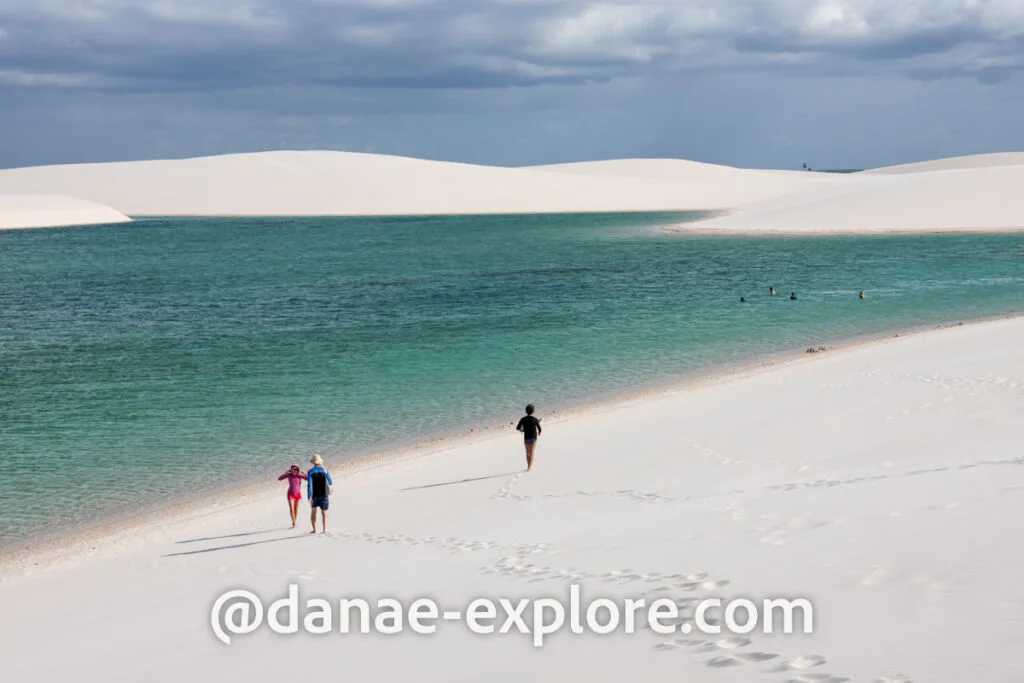 pessoas caminhando pelas dunas em direção à lagoa de águas everdeadas, em Lençóis Maranhenses
