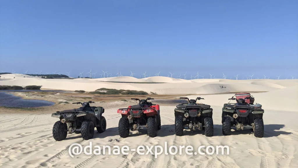 quadriciclos em cima de dunas, ao fundo se veem lagoas e turbinas eólicas, um dos passeios mais legais para se fazer em Lençóis Maranhenses