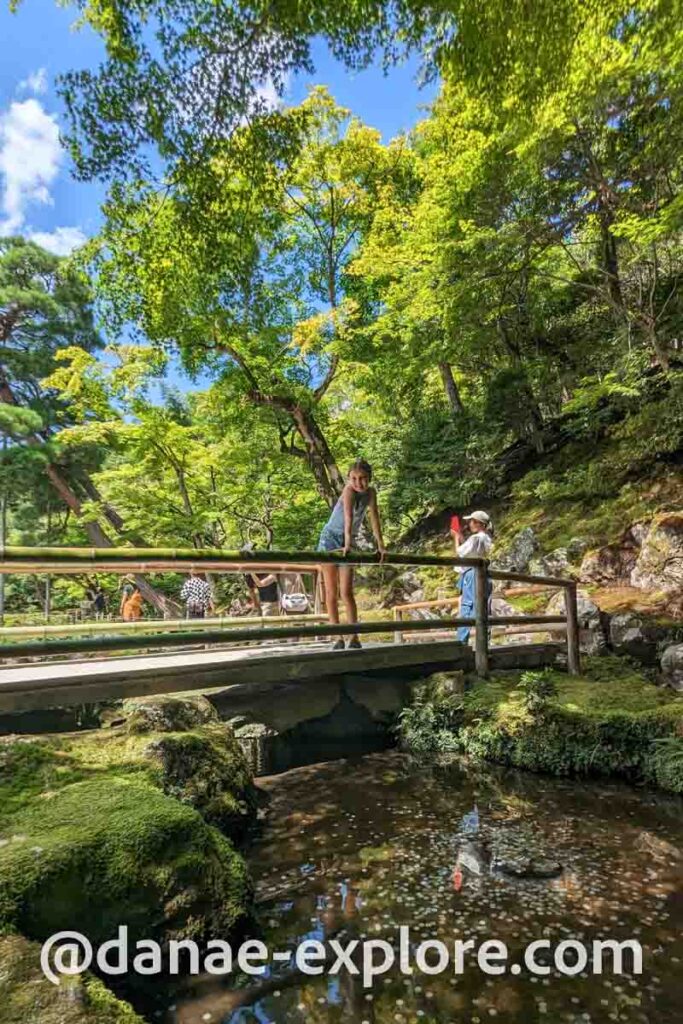 Menina em ponte nos jardins do Templo Ginkaku-ji, em dia de verão, em meio a vegetação verde