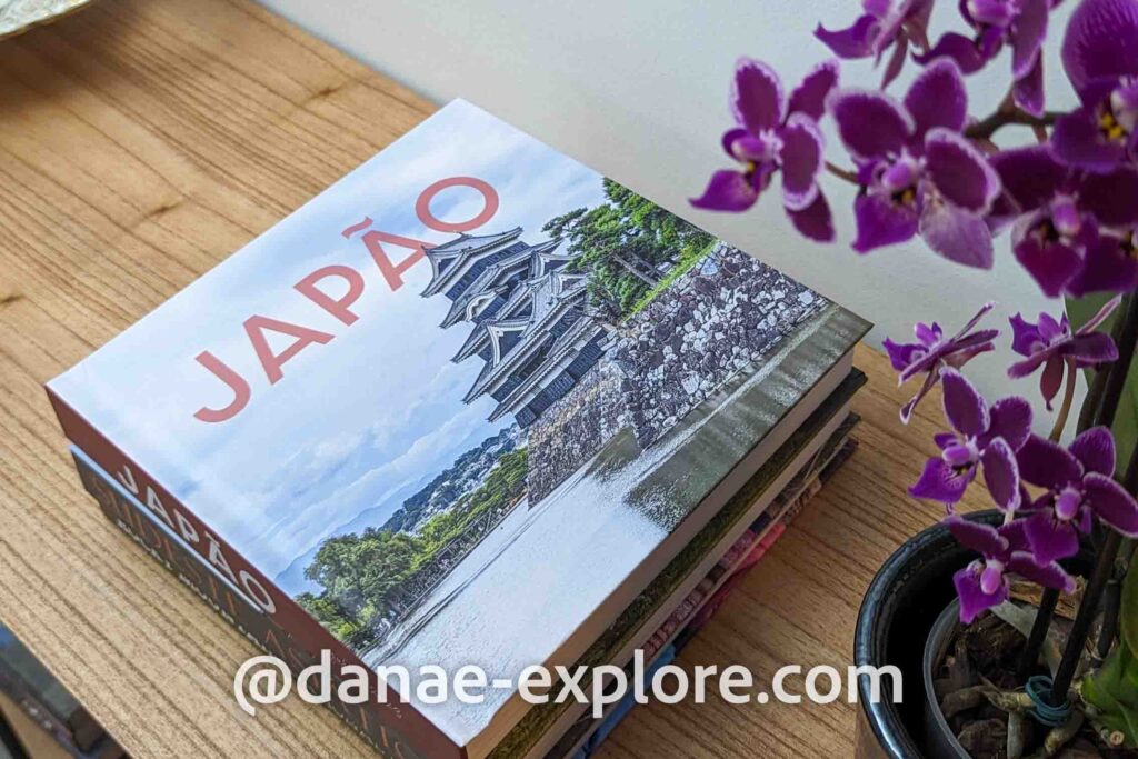 álbum de fotos da viagem ao Japão em cima de uma mesa; um vaso de orquídeas roxas está visível a direita da foto