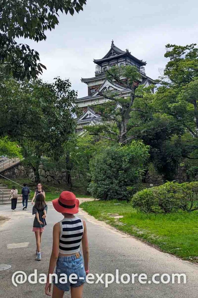 Castelo de Hiroshima, vista do parque. Há algumas pessoas de costas para câmera caminhando em direção ao Castelo