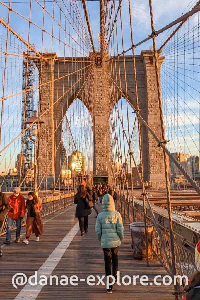 pessoas caminhando pela Brooklyn Bridge em dia de inverno, ao por do sol