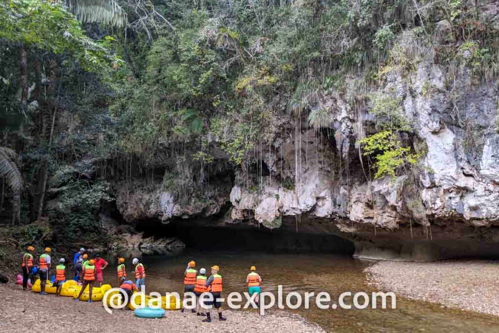 Grupo de pessoas com salva-vidas se preparam para entrar, com boias grandes, em rio que adentra caverna em Belize