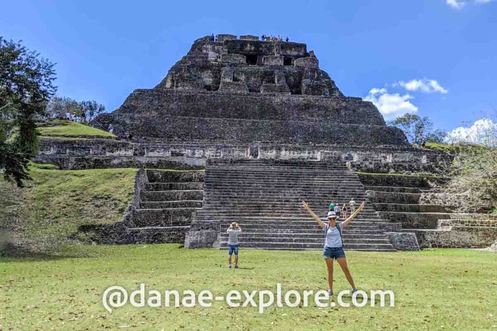 Moça em shorts, camiseta branca e chapéu, com braços erguidos em frente a El Castillo, nas ruínas maias de Xunantunich, sugestão de o que fazer em Belize