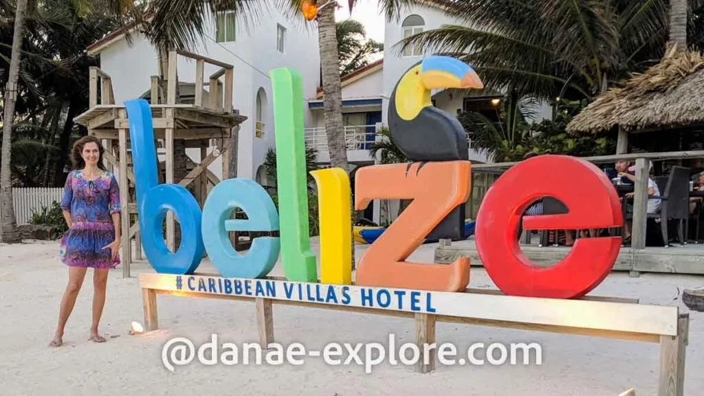 Girl in blue dress poses for camera next to sign that reads "belize" in letters