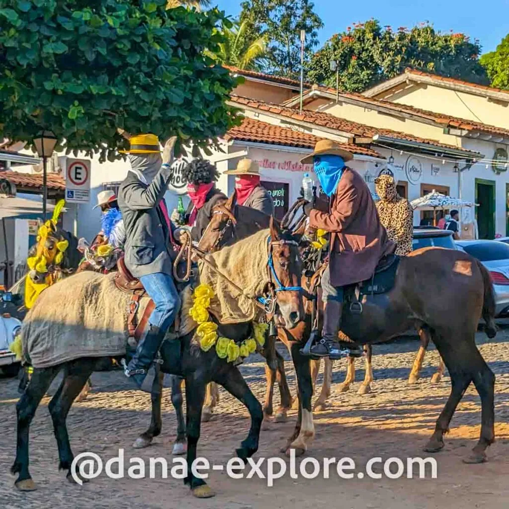 Cavalos enfeitados com flores e panos coloridos, montados por homens masccarados em chapéu e roupas coloridas, parte das Cavalhadas em Pirenopolis