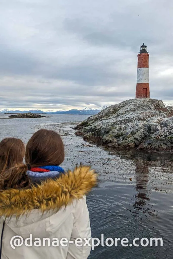 two girls, with their backs to the camera, observe the Les Eclaireurs Lighthouse, on a boat trip in the autumn on the Beagle Channel 