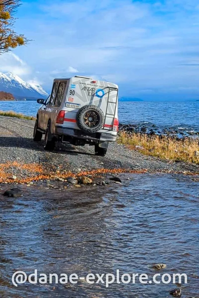 off-road vehicle on a road bordering a lake, in the background you can see mountains with snowy peaks