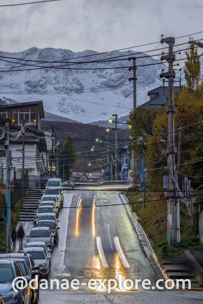 Ushuaia street in a cloudy late afternoon, you can see the trails of car headlights and snow-capped mountains in the background