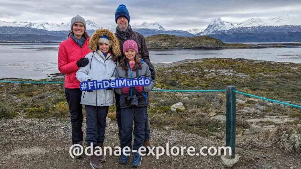 Family (couple and two girls) pose for a photo holding a sign that reads #findelmundo, at the Bridges Islands, one of the stops on the boat tour along the Beagle Channel