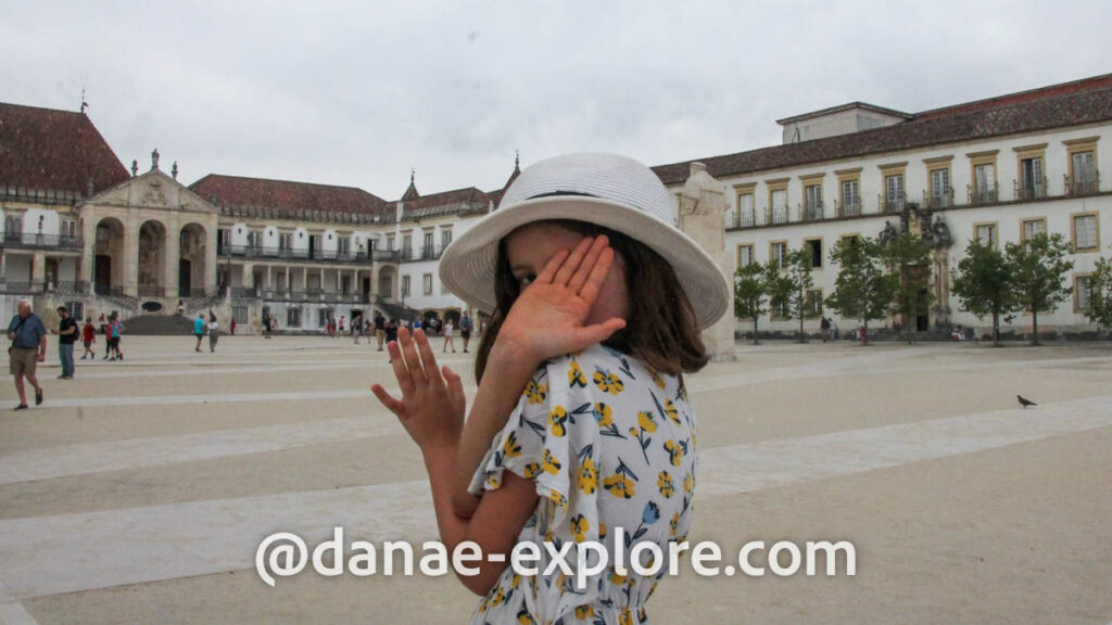 garota colocando as mãos no rosto para se esconder da câmera no pátio da Universidade de Coimbra, em dia de calor e céu nublado