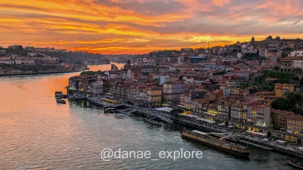 Sunset in Porto, in orange tones. In the foreground the river and to the right and in the background the city with some illuminated buildings and streets