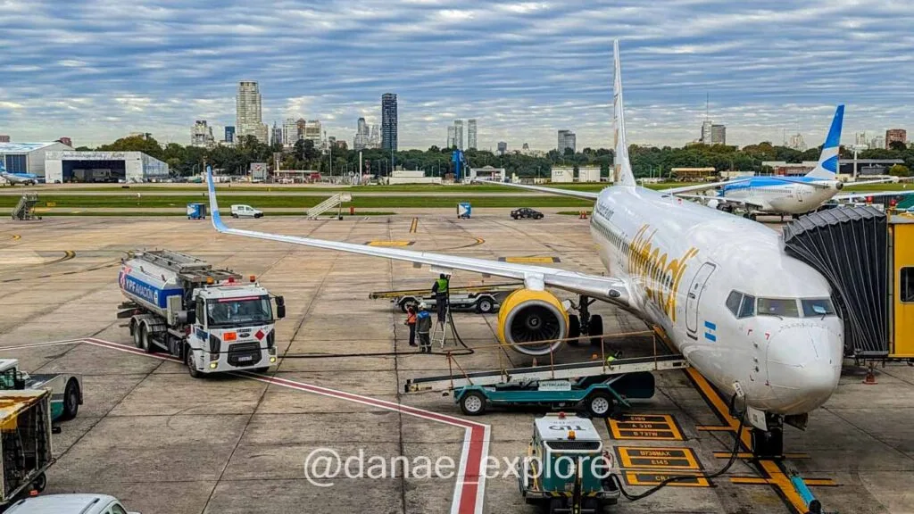 view of an airport runway, with an aircraft on the finger. In the background, the city of Buenos Aires, with tall buildings. It's a cloudy day