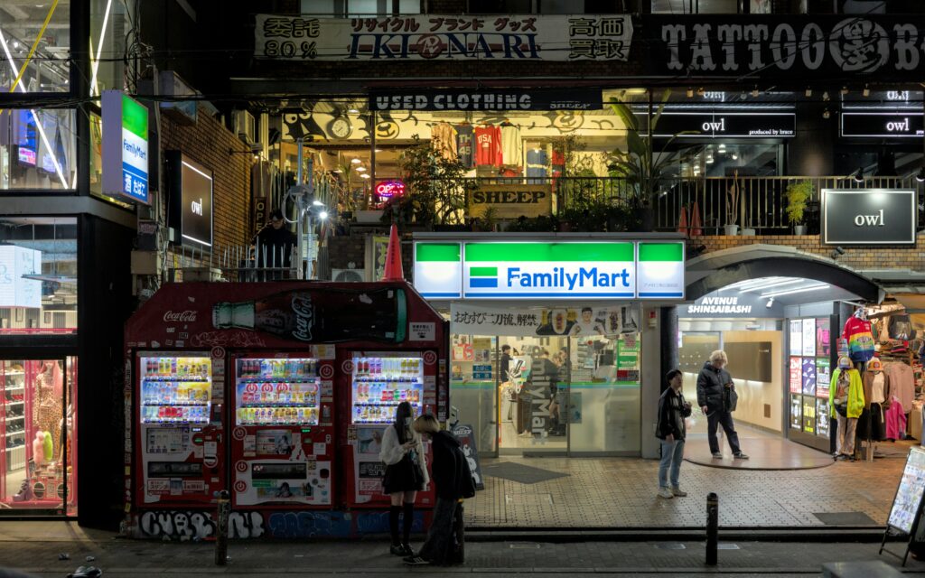 Cena noturna de Tóquio, com destaque para estação de metrô, loja de conveniência e máquinas de atendimento automático. Foto de Julien na Unsplash.