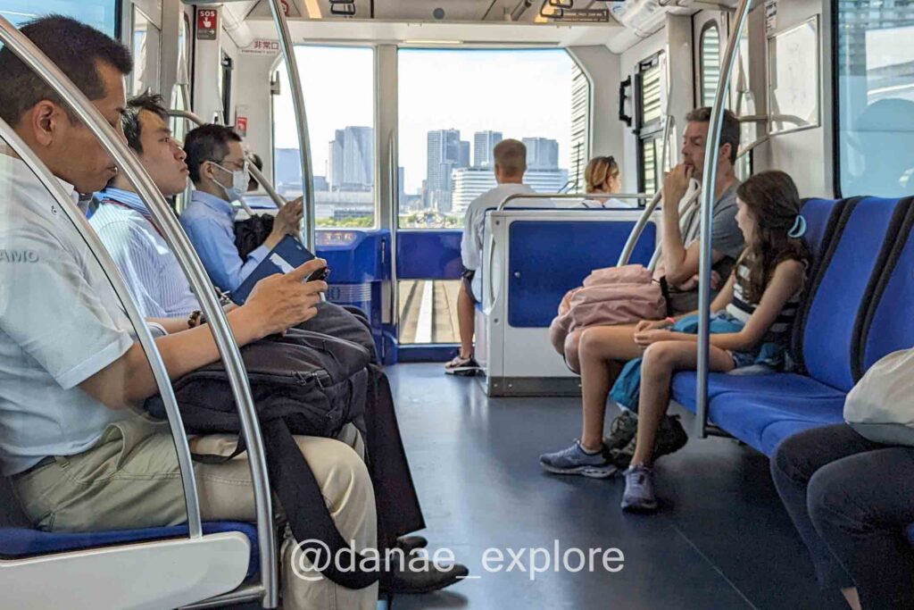 pessoas sentadas em trem do metrô em Tóquio, é possível ver prédios à distância
