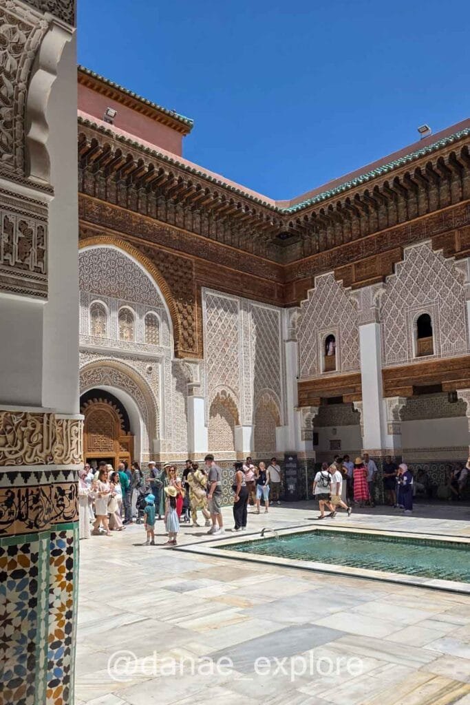 Marrakech – Ben Youssef Madrasa richly decorated with mosaics and intricate carvings, with several visitors exploring the site
