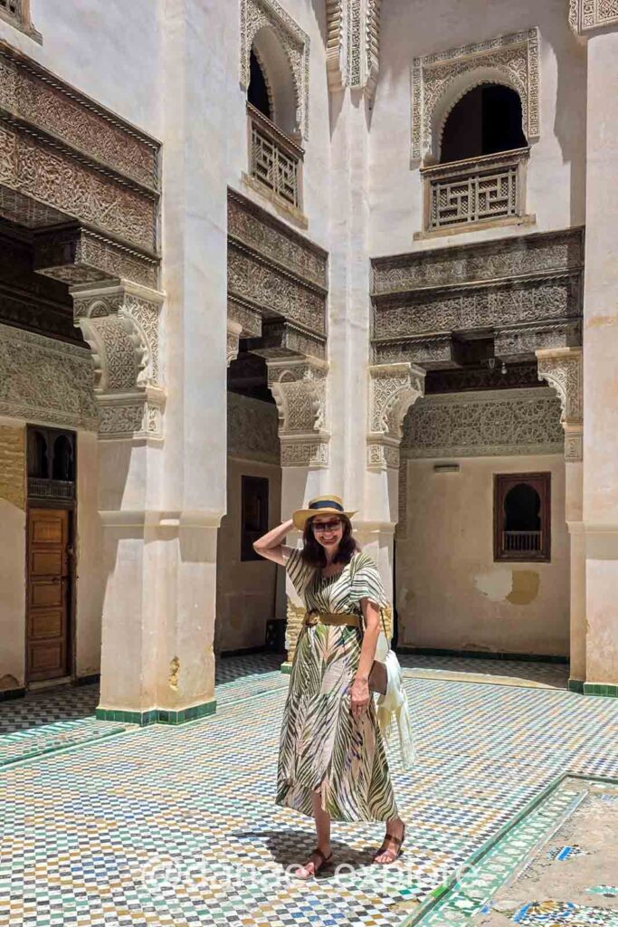 Moça em vestido longo e chapéu sorri para câmera na Madrassa Cherratine, em Fes, Marrocos - sugestão de o que vestir no Marrocos