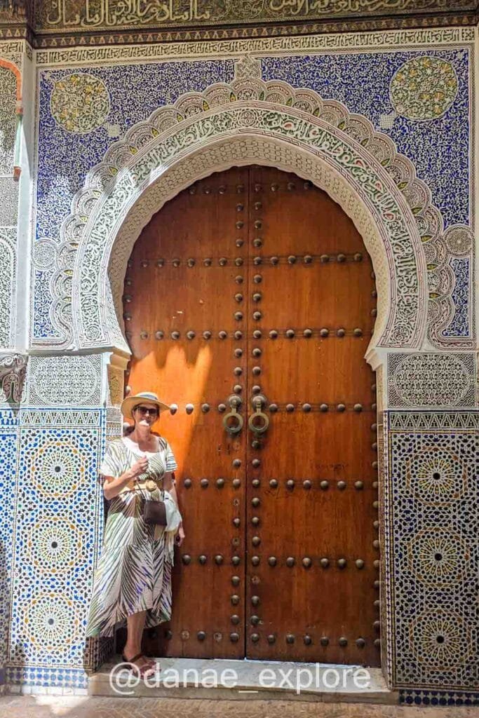 me, wearing dress and hat, in front of a door richly decorated with Moroccan motifs in the Medina of Fès
