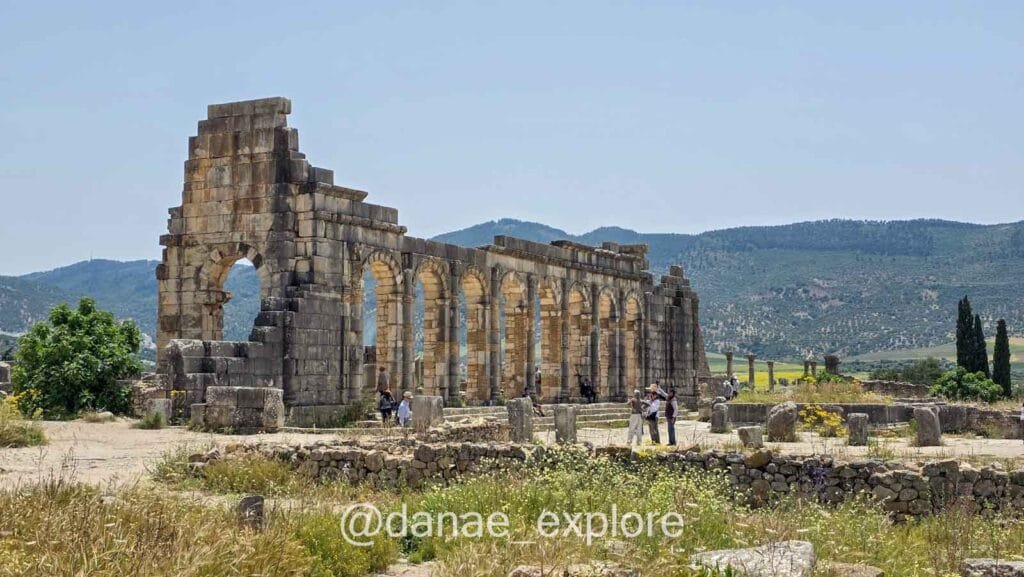 Panoramic view of the ruins of Volubilis, Morocco, on a clear day. Some tourists are visiting the site.
