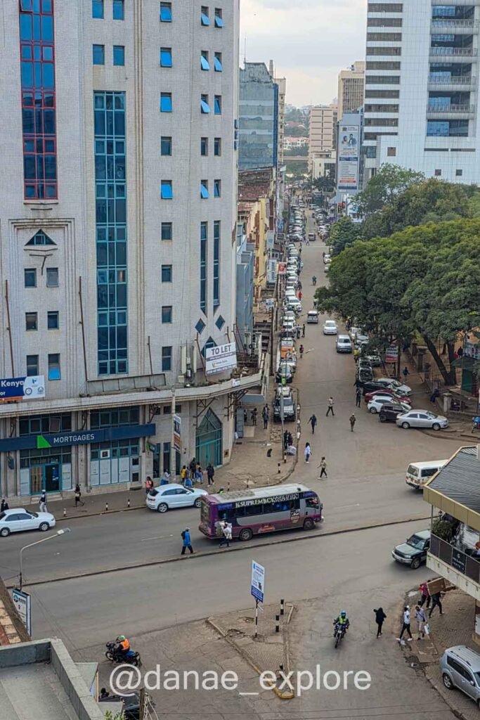 Vista aérea de rua em Nairobi, em dia claro. Há poucos carros na rua e algumas pessoas caminhando.