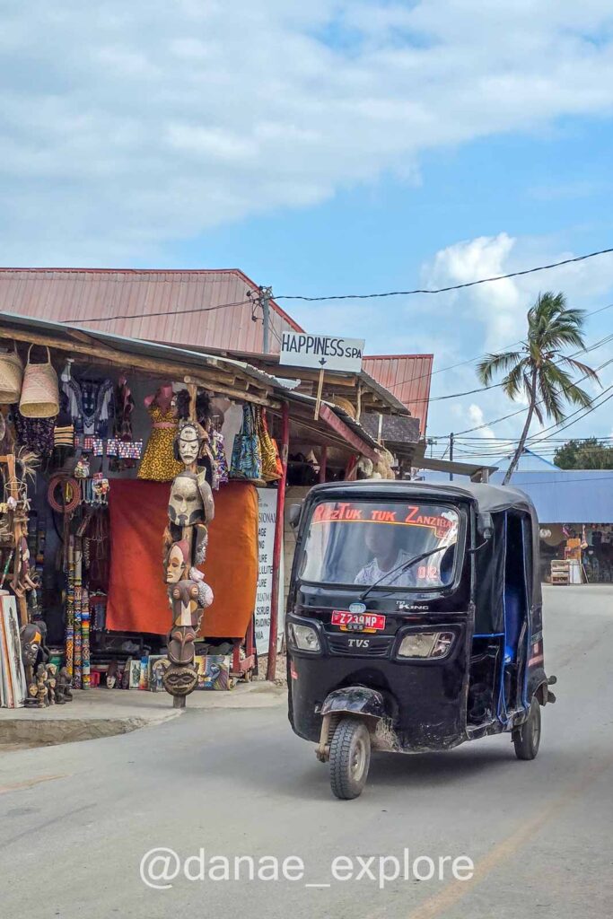 tuc-tuc preto em rua com lojas de artesanato em Nungwi, Zanzibar
