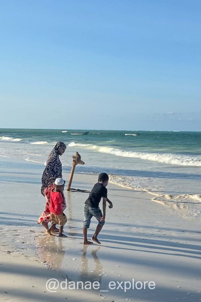 mulher em trajes islâmicos, com hijab, brinca com crianças na praia em Paje, durante nossa viagem por Zanzibar