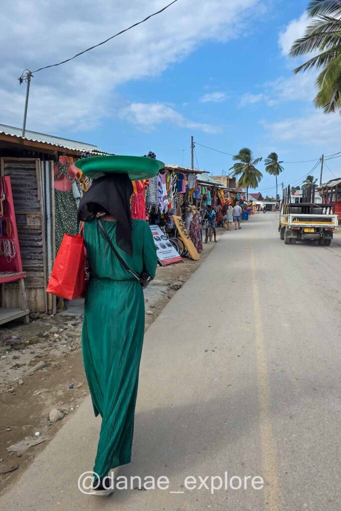 mulher em vestido longo e hiyab caminha em rua com lojas de artesanato em Nungwi, Zanzibar