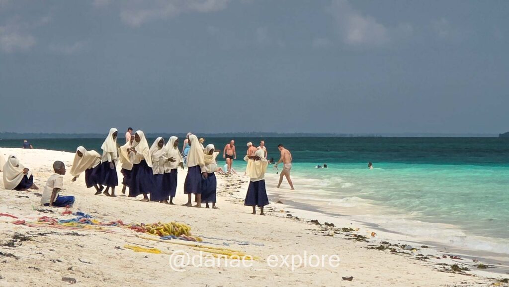 Meninas em saia longa azul, blusa branca e lenço islâmico al-amira brincam na praia Kendwa, parte de nosso roteiro em Zanzibar