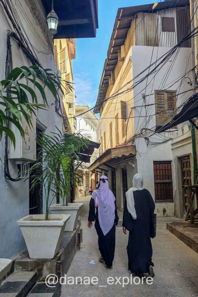 Duas mulheres em trajes islâmicos caminham, afastando-se da câmera, em rua de Stone Town, parte de nosso roteiro de Zanzibar