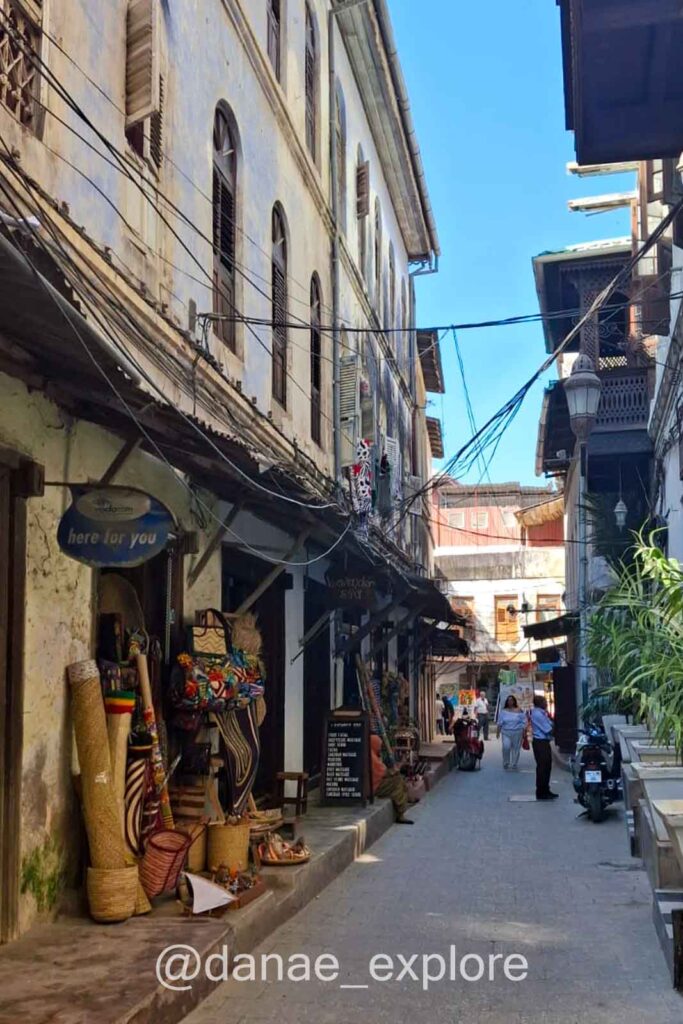 ruela de Stone Town com prédios baixos e lojas de souvenirs no térreo