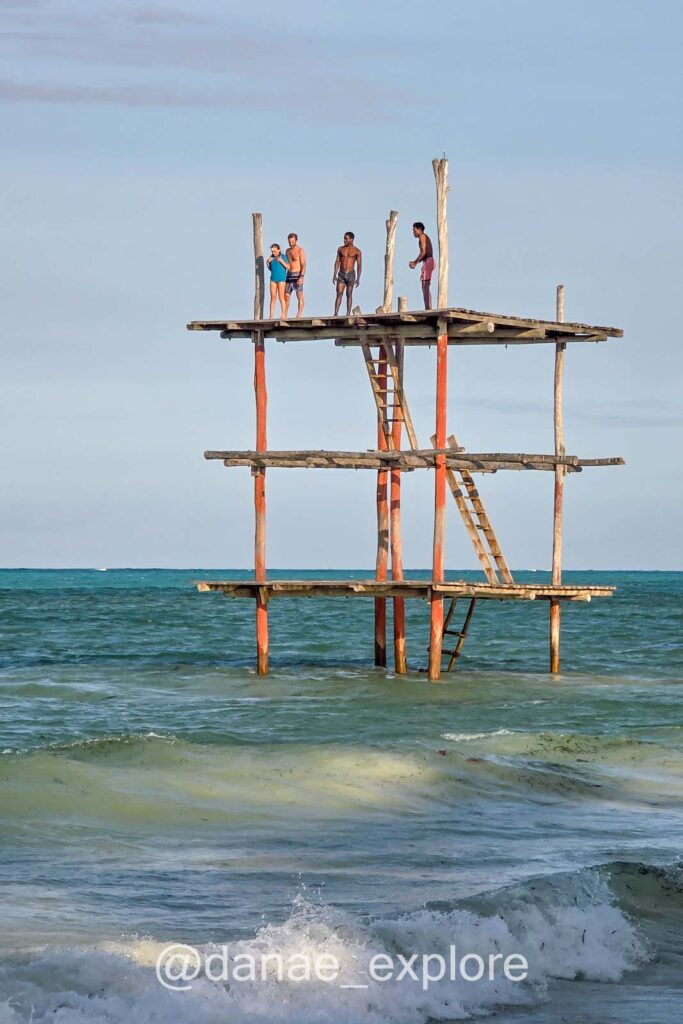 Plataforma de madeira com três pavimentos na praia de Bwejuu - Paje durante a maré alta. O mar cobre praticamente todo o primeiro pavimento da plataforma. Há quatro pessoas no úlimo patamar da plataforma