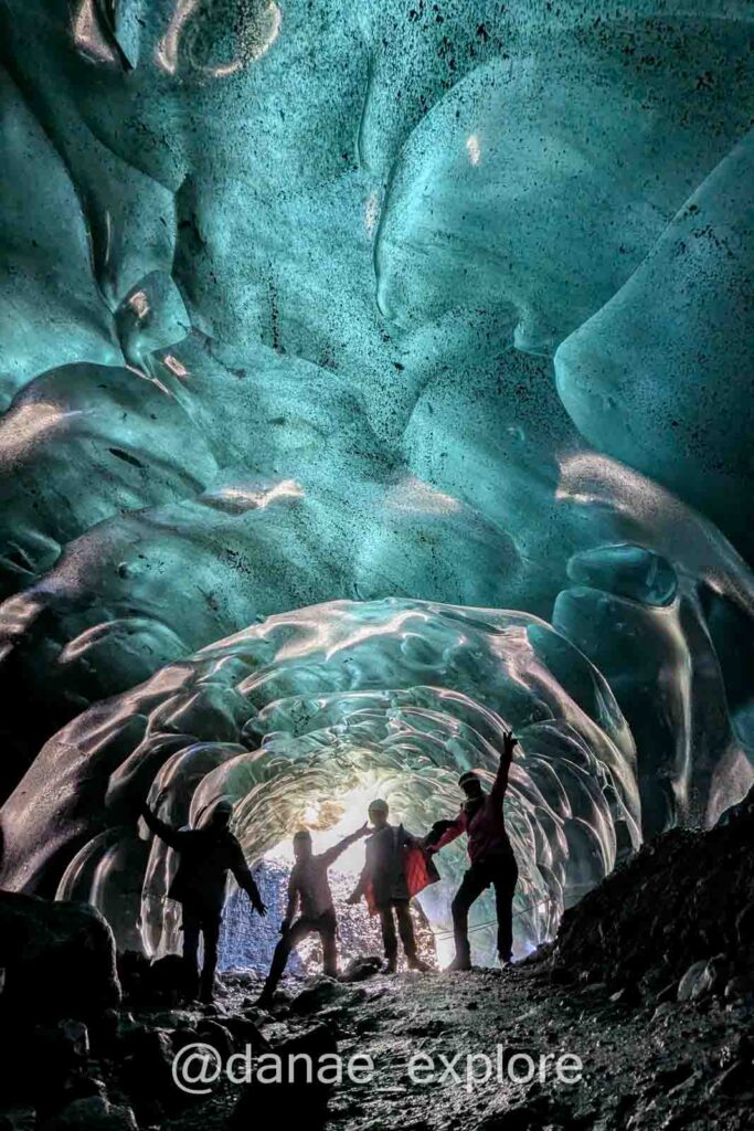 Grupo de pessoas posa dentro de uma caverna de gelo azul na Islândia, em contra-luz, com luz natural iluminando as paredes de gelo, que tem coloração verde-azulado. Foi o ponto alto de nossa viagem pela Islândia