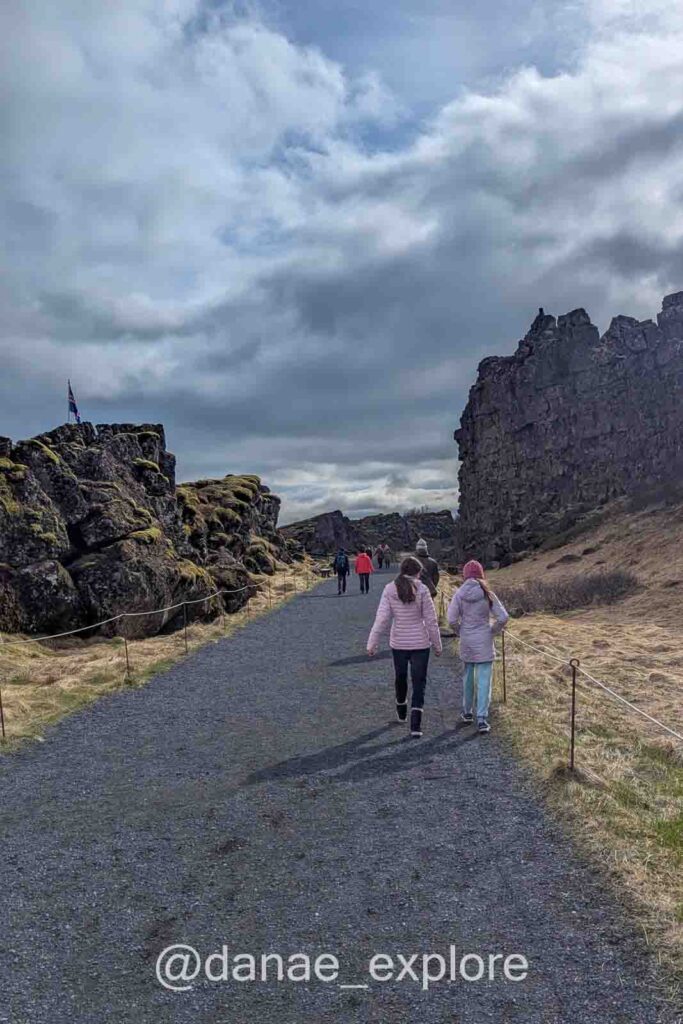 Pessoas caminham por uma trilha entre paredões rochosos cobertos de musgo no Parque Nacional Þingvellir, na Islândia. O caminho marca a fenda entre as placas tectônicas da América do Norte e da Eurásia