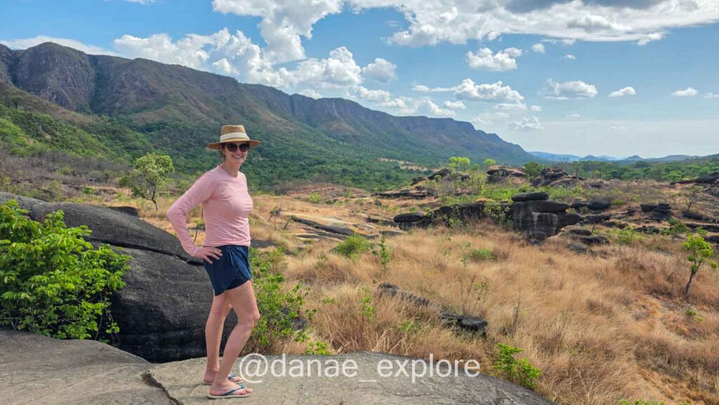 Estou vestindo shorts azul e camiseta rosa de manga longa, chapéu e óculos de sol em mirante na trilha do Vale da Lua, na Chapada dos Veadeiros, próximo a São Jorge.