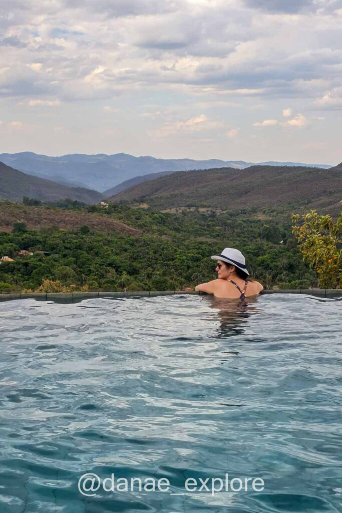 Eu estou na piscina de borda infinita da Pousada Vila Toá, com vista panorâmica para as montanhas da Chapada dos Veadeiros ao entardecer.