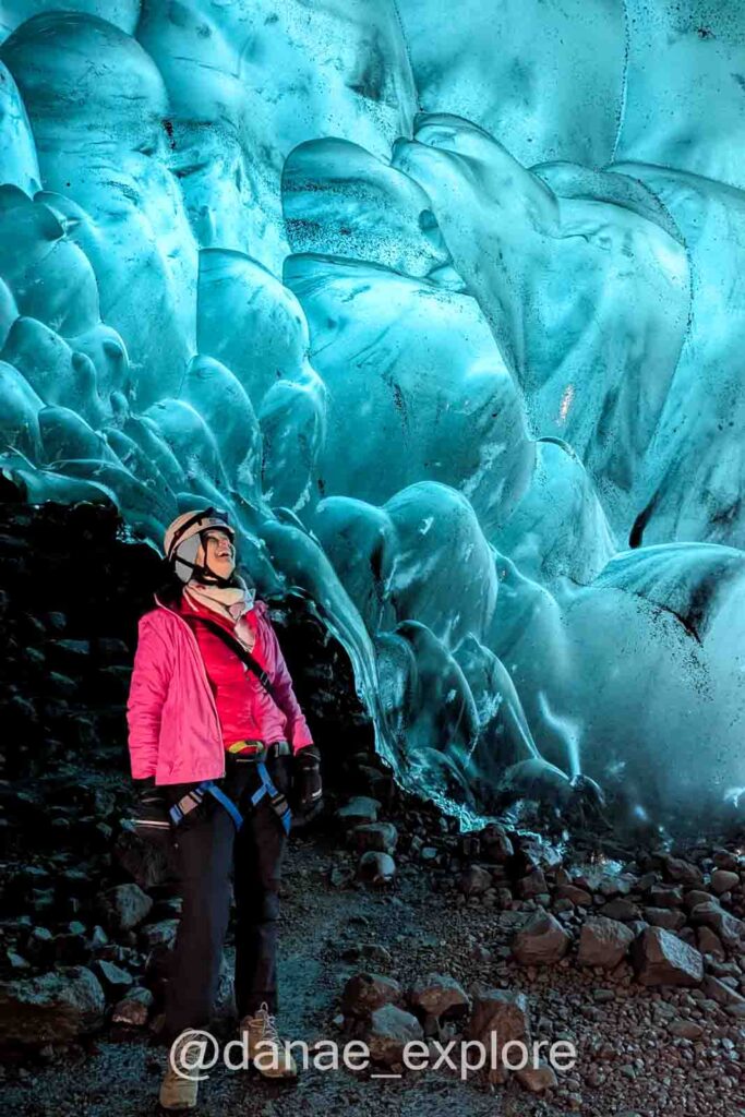 Eu, com blusa rosa e capacete, observando o interior azul da caverna de gelo no Vatnajökull